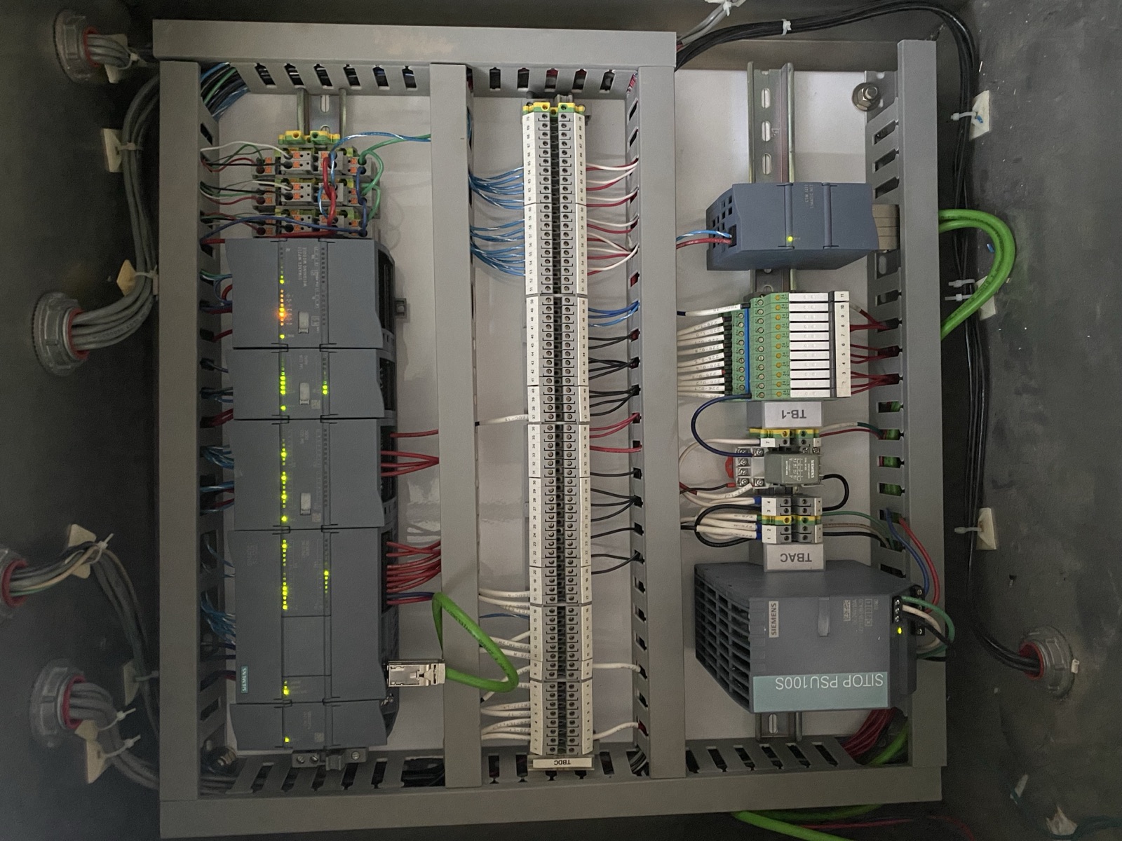 The same panel with a current S7-1200 PLC, labeled terminals and a SITOP power supply